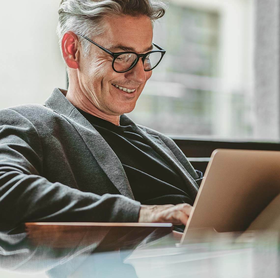 Man with glasses sitting and smiling at his computer.