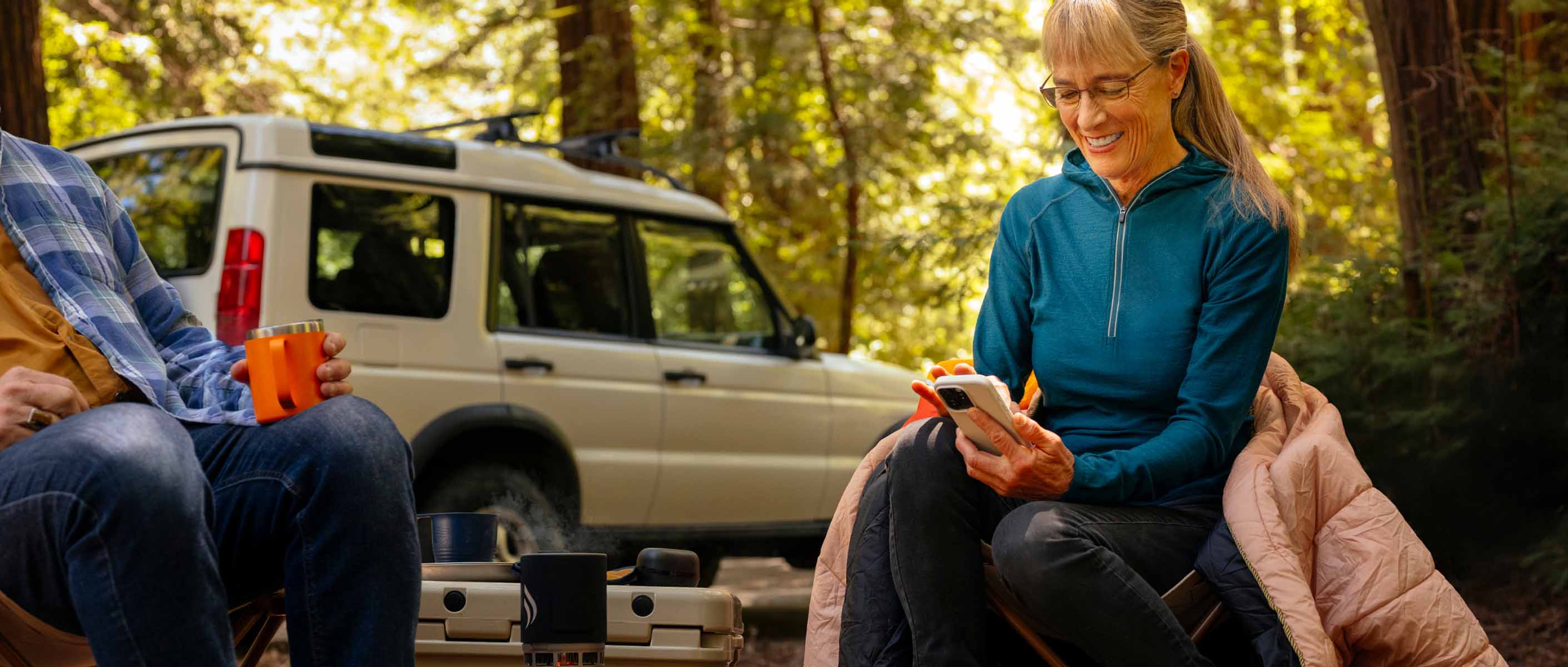Daphne sitting in a camping site looking at her phone and smiling.