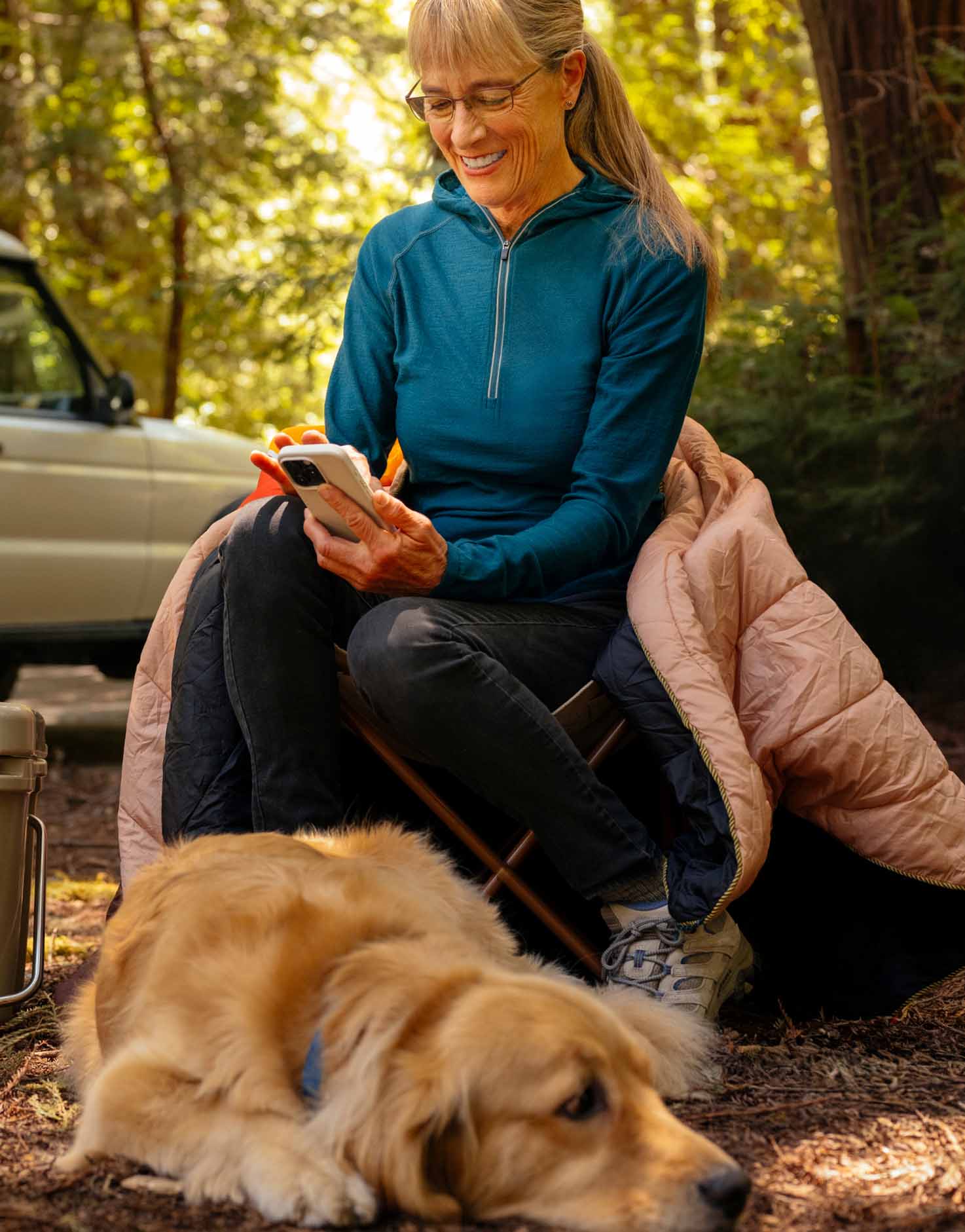 Daphne sitting in a camping site looking at her phone and smiling.